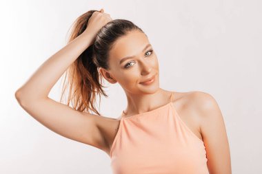 Güzel esmer bir kız saçını tutup kendi saç stilini yapar. Uzun saçlı, gri arka planda turuncu giysili genç bir manken. Kadın gülümser ve kameraya bakar.