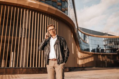 Büyük bir şehrin caddesinde gözlüklü, akıllı telefonlu yakışıklı bir adam. İş adamı şehir planıyla ilgili telefonda konuşuyor.