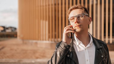 Büyük bir şehrin caddesinde gözlüklü, akıllı telefonlu yakışıklı bir adam. İş adamı şehir planıyla ilgili telefonda konuşuyor.