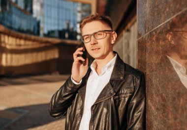 Büyük bir şehrin caddesinde gözlüklü, akıllı telefonlu yakışıklı bir adam. İş adamı şehir planıyla ilgili telefonda konuşuyor.