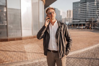 Büyük bir şehrin caddesinde gözlüklü, akıllı telefonlu yakışıklı bir adam. İş adamı şehir planıyla ilgili telefonda konuşuyor.