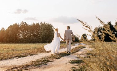 Düğün günü gelin ve damat gün batımında ormana doğru yol boyunca sarılıp yürüyorlar.