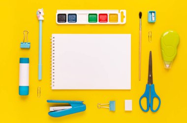 Modern beyaz, mavi, sarı ofis masaüstü, okul gereçleri ve kırtasiye malzemeleriyle dolu. Masanın etrafında mesaj için boş alan var. Okula dönüş konsepti dairesi modelle yatıyordu.