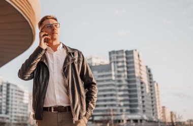 Büyük bir şehrin caddesinde gözlüklü, akıllı telefonlu yakışıklı bir adam. İş adamı şehir planıyla ilgili telefonda konuşuyor.