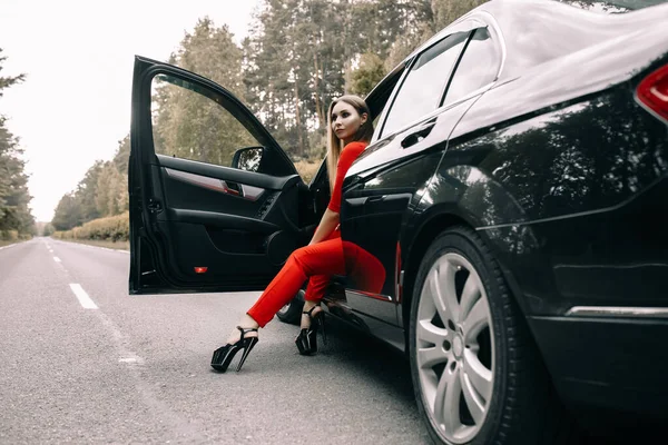 Piękna Młoda Dziewczyna Czerwonym Kombinezonie Siedzi Kierownicą Czarnego Samochodu Pustej — Zdjęcie stockowe