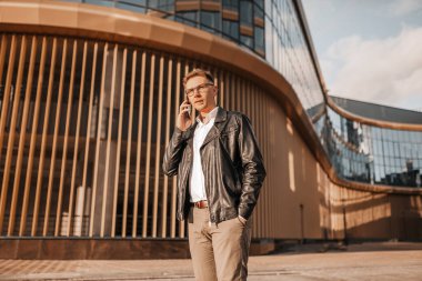 Büyük bir şehrin caddesinde gözlüklü, akıllı telefonlu yakışıklı bir adam. İş adamı şehir planıyla ilgili telefonda konuşuyor.