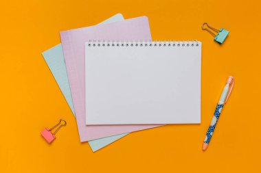 Not defteri, egzersiz kitabı ve kalem masaya. Fotokopi odasında turuncu arka planda. Okula geri dön.