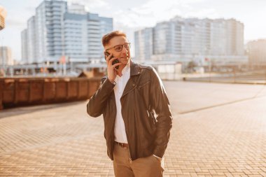 Büyük bir şehrin caddesinde gözlüklü, akıllı telefonlu yakışıklı bir adam. İş adamı şehir planıyla ilgili telefonda konuşuyor.