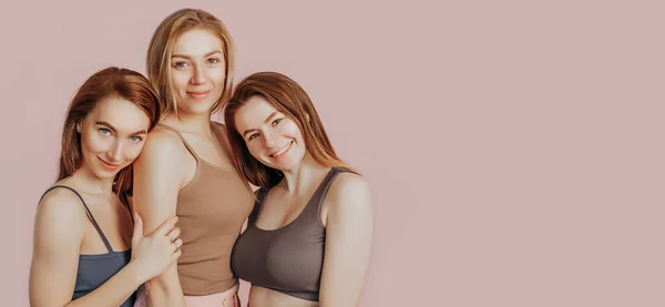 ピンクの背景に快適な家庭服を一緒に3人の女の子 女性は笑顔で楽しんでいます スパトリートメント 自然の美しさとケア クリームとマスク 新鮮さ 友情の概念 — ストック写真