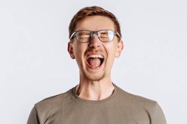 Gözlüklü, sakallı, genç, yakışıklı esmer adam çaresizlik içinde çığlık atıyor ve beyaz tenli arka planda mutsuz.