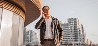 Büyük bir şehrin caddesinde gözlüklü, akıllı telefonlu yakışıklı bir adam. İş adamı şehir planıyla ilgili telefonda konuşuyor.