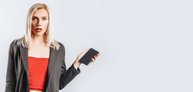 Güzel, genç ve mutsuz bir kız. Gri arka planda telefonu tutuyor.