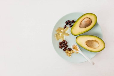 Sağlık ve diyet konsepti. Avokado ve kapsüllerdeki balık yağı D vitamini ve beyaz arka plandaki bir tabakta omega-3 yağ asitleri için.