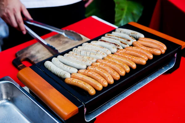 Salsicha fresca e cachorros-quentes grelhando ao ar livre em um churrasco a gás — Fotografia de Stock