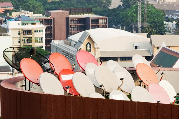 Um pássaro senta-se na antena parabólica com outros pratos borrados no th — Fotografia de Stock