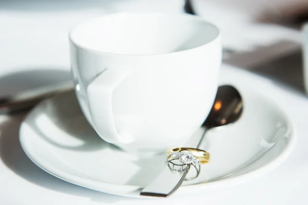 Filiżanka kawy, ślub pierścienie w łyżką na stole — Zdjęcie stockowe