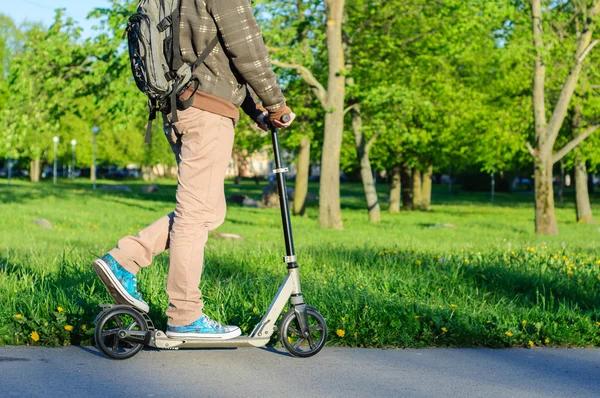 Young man in casual wear on kick scooter in park