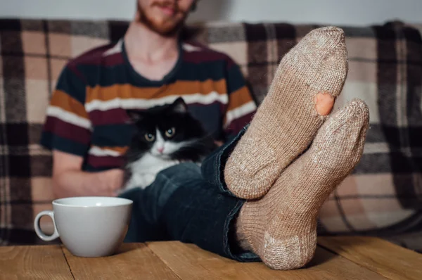 Young man sitting on couch with cat in holey socks