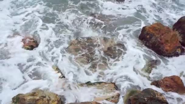 Голубые волны черного моря, бьющиеся коричневыми камнями. Вид сверху на море с пеной — стоковое видео