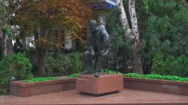Yalta - 18 Kasım 2020: Parkta sandalyede oturan bir adam için anıt. Yeşil ağaçlar ve çiçek yataklarıyla çevrili