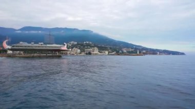 Yalta - 18 Kasım 2020: şehir kıyılarının panoraması. Deniz, dağlar, gökyüzü. Denizin üzerinde uçan kuşlar, sahil, bina suyun yanındaki eski iskelede duruyor.