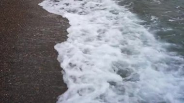 Denizin taş kıyısı deniz dalgası tarafından yıkanır. Köpük yuvarlanıyor