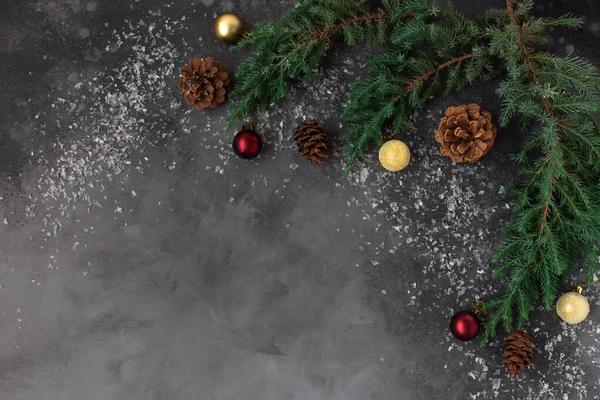 Fond plat de Noël avec des décorations de branches de sapin, cônes et boules de Noël sur un fond sombre avec de la neige. espace libre pour le design — Photo
