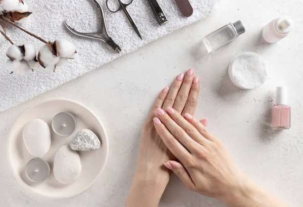 set of manicure tools and well-groomed female hands with natural manicure. manicure at home. White concrete background, flat lay.