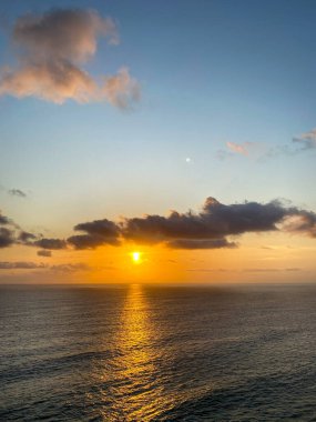 Deniz üzerinde gün batımı manzarası, turuncu, kırmızı ve mavi renklerle güzel bir siluet yaratıyor..