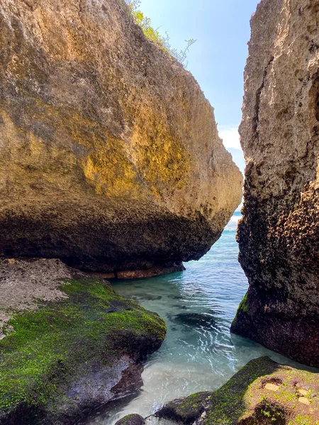 Sahilde büyük bir kaya oluşumu, küçük bir mağarası, sakin deniz dalgaları..