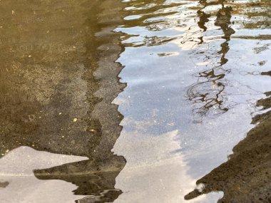 Bir alışveriş merkezinin çeşme alanında su yüzeyi ışık yansımaları ve bina yapıları ile çevrili..