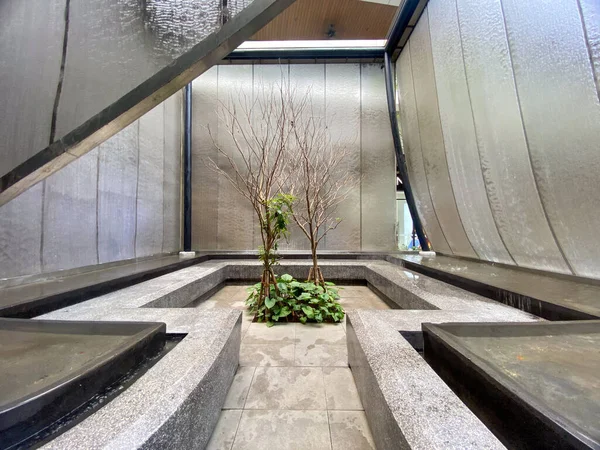 Duvardan aşağı süzülen, küçük yeşilliklerle çevrili modern taş çeşme..