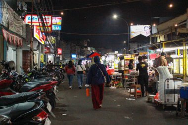 Jakarta, Endonezya - 27 Kasım 2025: İnsanlar ALFAMART mağazaları ve sokak yiyecek tezgahları tarafından çevrelenmiş kalabalık bir gece marketinde yürüyorlar.