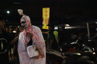 Jakarta, Endonezya - 27 Kasım 2025: Kan sıçramış hayalet kostümlü bir adam kalabalık bir otoparkta gece pazarında duruyor..