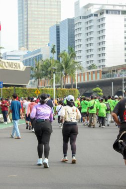 Jakarta, Endonezya - 27 Kasım 2025: Kalabalığın arasında yürüyen ve çoğu Sudirman Merkez Jakarta 'da Yeşil Arabasız Günü tişörtü giyen iki kadın.