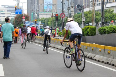 Bir grup vatandaş bisiklet sürüyor ve hafta sonları arabasız bir şeritte yürüyor. Bisikletçi ön planda kask takıyor..
