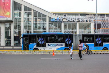 Jakarta, Endonezya - 27 Kasım 2025: Transjakarta Volvo V8400L Mavi Otobüs ve Thamrin, Jakarta 'da bir bisikletçi önünde yürüyen bir erkek ve bir kadın.