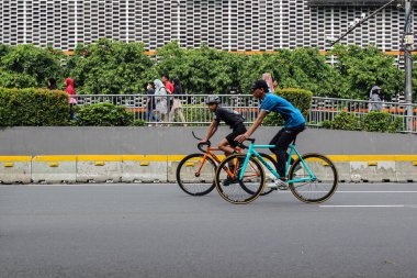 Jakarta, Endonezya - 27 Kasım 2025: İki erkek bisikletçi, Bawaslu inşaat duvarının önündeki otoyolda sabit vites bisikleti sürüyor, Jakarta.
