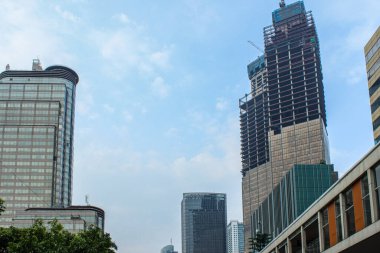 Modern gökdelenlerin manzarası, Jakarta şehrinin merkez iş bölgesinde inşaat halindeki bir bina, mavi gökyüzü ve beyaz bulutlar.