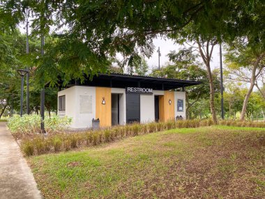 Siyah çatılı ve ahşap aksanlı küçük modern umumi tuvalet binası, PIK 2 parkının ortasında ağaçlarla çevrili bir 