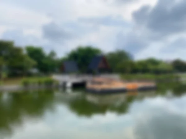 The abstract background is out of focus. Two black-roofed gazebos and pier decks over the water, surrounded by green trees reflecting on the calm lake surface.
