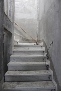 Açık gri mermer kaplı, düz beton duvarlı ve monte edilmemiş elektrik kablolarıyla kaplı kapalı merdivenler yenileme sürecinde..