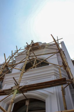 Yapım aşamasındaki klasik bir lüks evin ön kulesinin alçak açılı görüntüsü, parlak gökyüzüne ulaşan bambu iskele ağıyla güçlendirilmiş..
