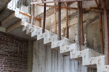 Tamamlanmamış beton merdiven, pürüzlü doku, boyanmamış duvarlar, geçici ahşap ve demir parmaklık inşaatı..