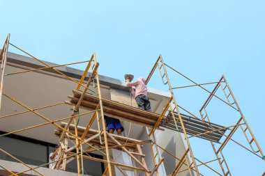 Jakarta, Endonezya - 11 Aralık 2025: Uzun metal iskelelerde inşaat işçisi, alçak açılı bir çekimle görülen modern minimalist bir evin çatısında sıva veya bitirme işi yapıyor.