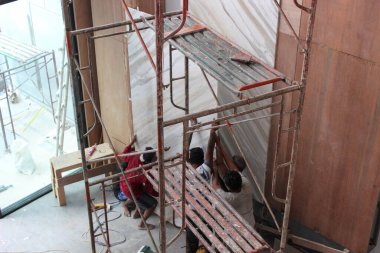 Jakarta, Endonezya - 11 Aralık 2025: İnşaat işçileri iç duvarda gri çapraz damar desenleri olan büyük bir beyaz mermer levhayı kaldırmak ve kurmak için yapı iskelesi kullanıyorlar.