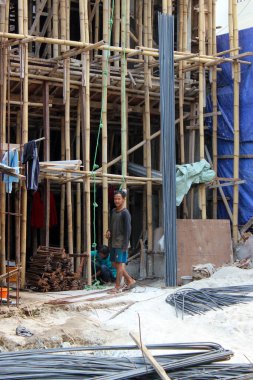 Jakarta, Endonezya - 11 Aralık 2025: Endonezya 'da inşaat işçisi, inşaat malzemeleri hazırlama sürecinde yer alan bir inşaat inşaat iskelesi ve beton yığınının yanında duruyor.