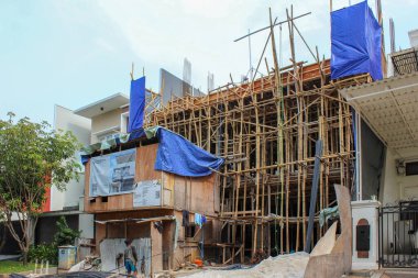 Jakarta, Endonezya - 11 Aralık 2025: Modern ev inşaatı, lüks bir semtteki diğer modern evlerle çevrili büyük geleneksel bambu iskelesi ve mavi muşambaları kullanıyor.