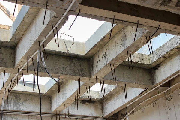 Unfinished concrete roof structure with skylight-like gap openings, concrete beams, and numerous steel reinforcements on a construction project.