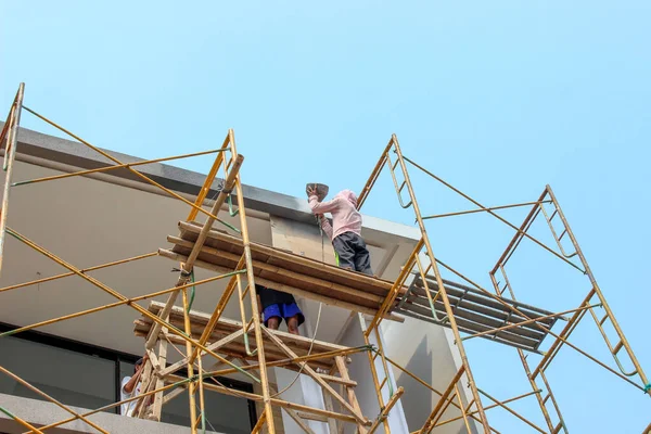 Jakarta, Endonezya - 11 Aralık 2025: Uzun metal iskelelerde inşaat işçisi, alçak açılı bir çekimle görülen modern minimalist bir evin çatısında sıva veya bitirme işi yapıyor.